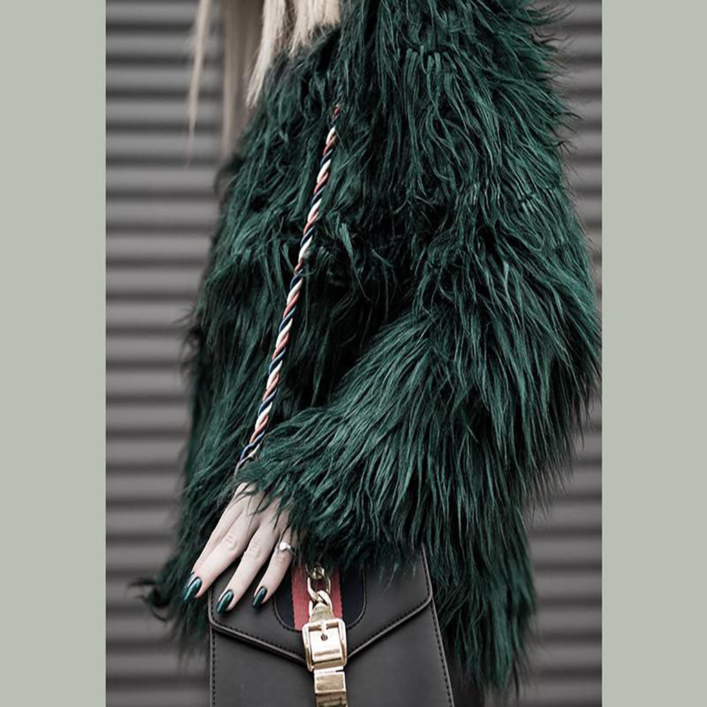 Woman wearing a green furry coat with a black bag